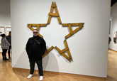 Karlo Andrei Ibarra stands next to his star, or estrella, made from wooden police protest barricades at the USF Contemporary Art Museum. - Jessica Meszaros / WUSF